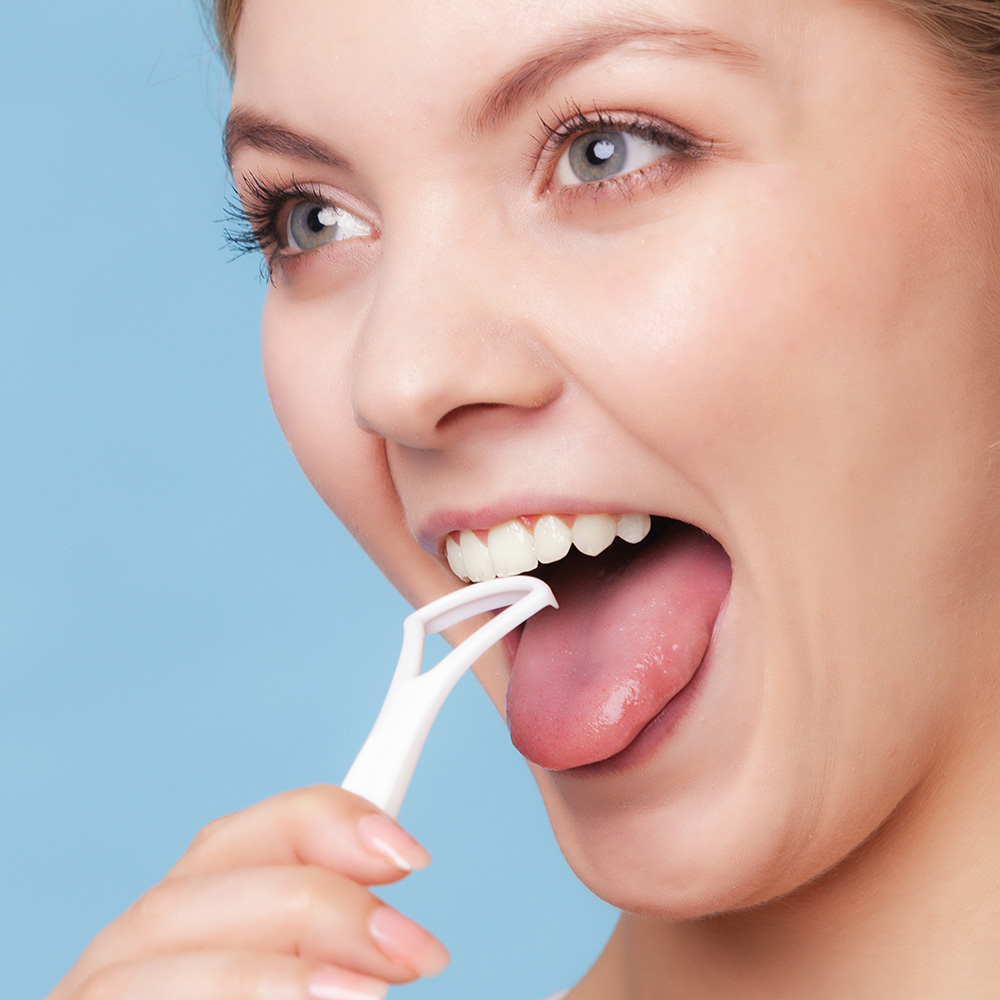 Die Reinigung der Zunge sollte ganz selbstverständlich zu Ihrer normalen Zahnputzroutine gehören. Eine Frau zeigt die Anwendung einer Zungenbürste.